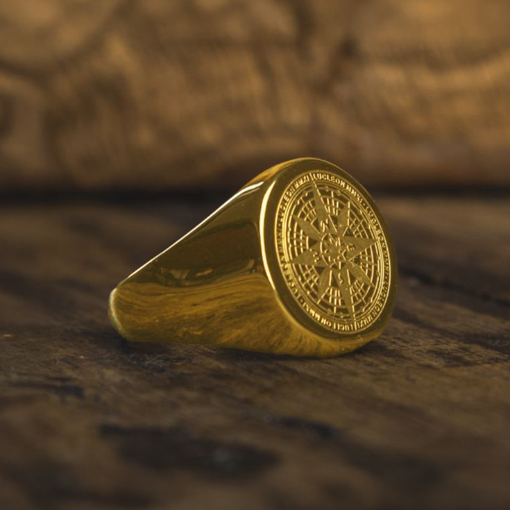 Bague boussole pirate dorée en acier inoxydable posée sur un bois vieilli, bijou corsaire au style vintage évoquant les trésors et la navigation maritime.