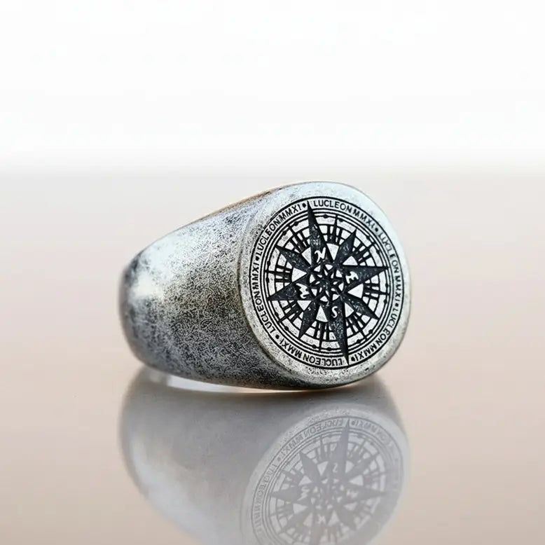 Bague boussole argentée posée sur fond blanc, vue produit épurée.