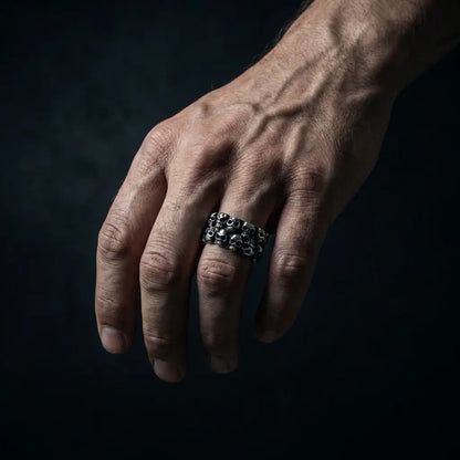 Bague des Crânes Liés portée à la main dans une atmosphère obscure et dramatique.