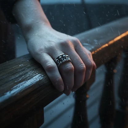 Main d’une femme portant la Bague Empire des Crânes sur le pont d’un navire, ambiance sombre.