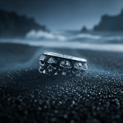 Bague Empire des Crânes posée sur un sol humide et sombre, éclairage dramatique bleu.