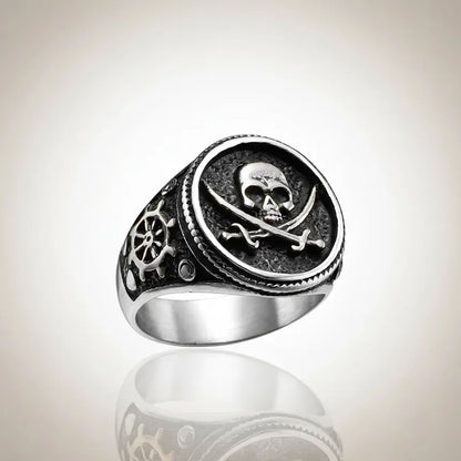 Bague du flibustier maudit en acier 316L finition argentée sur fond clair, design tête de mort et sabres croisés.