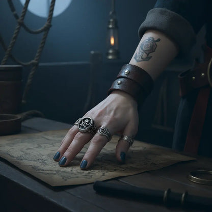 Bague du flibustier maudit portée sur une main de femme posée sur une carte au trésor, dans une cabine de navire.