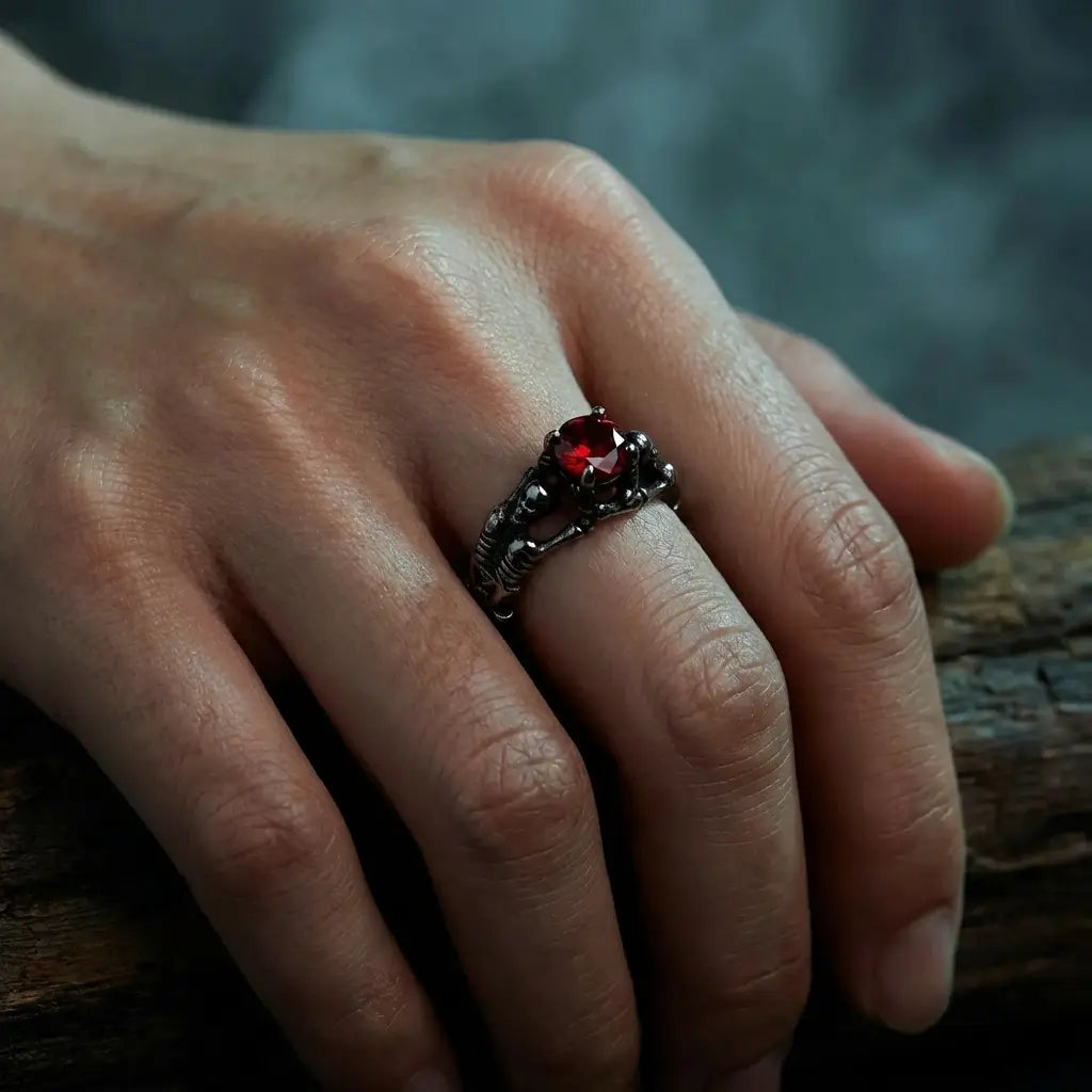 Bague du Pacte Scellé argentée avec la pierre rouge, portée sur la main dans une ambiance sombre.