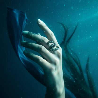 Main émergente dans l’eau portant la bague des tentacules argentées, atmosphère abyssale.