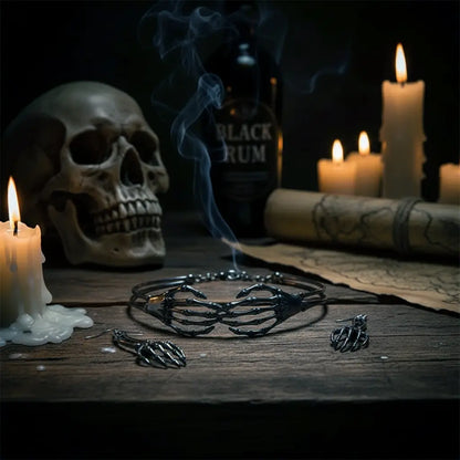 Collier et boucles d’oreilles gothiques en forme de mains squelettes posés sur une table sombre, ambiance Ténèbres avec crâne et bougies.
