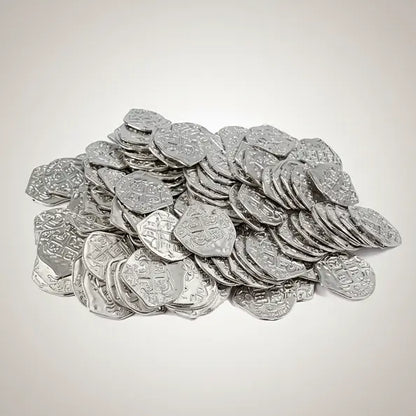 Lot de pièces pirates argentées sur fond clair, surface brillante et reliefs gravés.