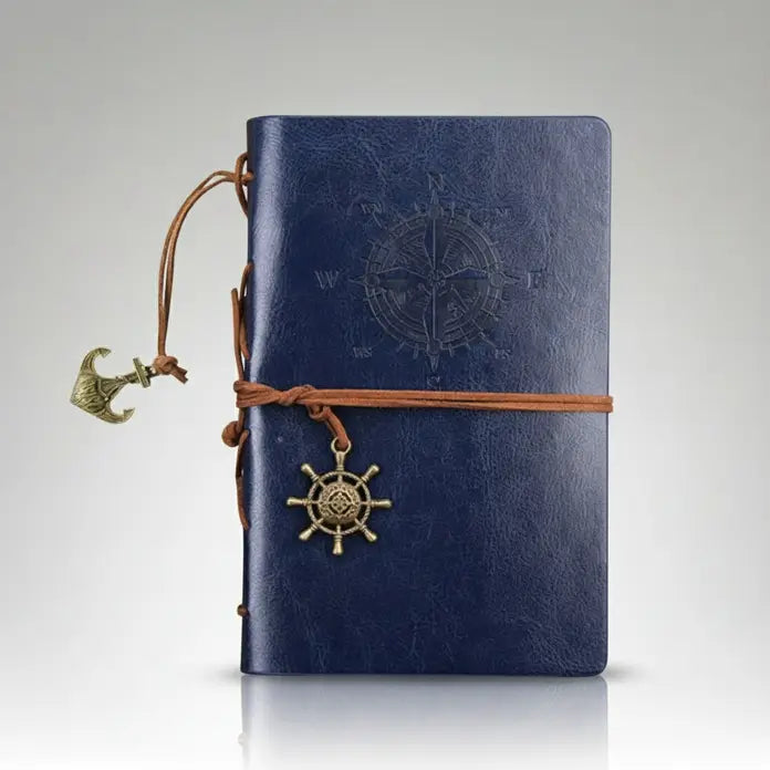 Carnet de pirate en cuir bleu avec spirale rigide et boussole gravée sur la couverture, style vintage marin.