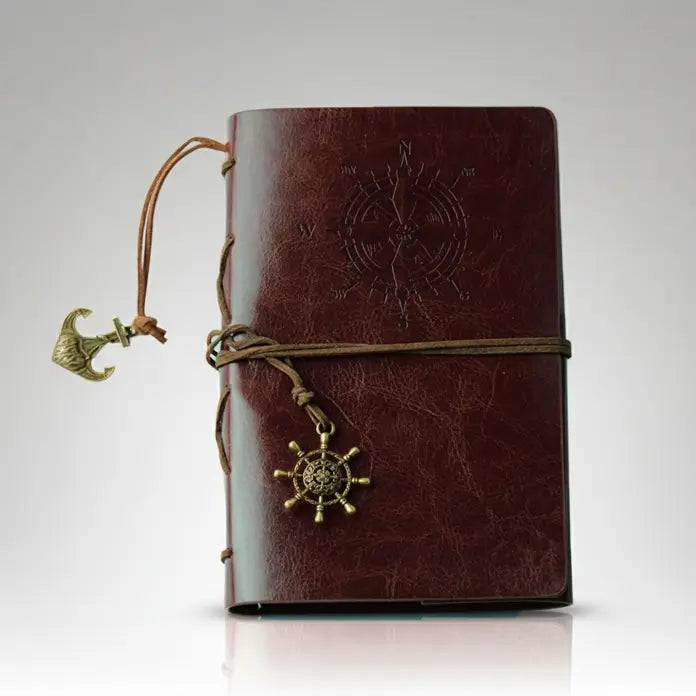 Carnet pirate en cuir marron avec spirale rigide et boussole embossée, aspect vieilli et élégant.