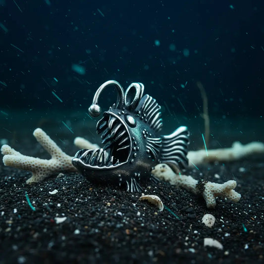 Collier Poisson Squelette Lanterne argenté posé sur le sable marin avec coquillages et coraux.