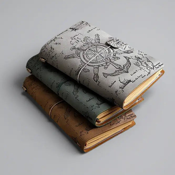Collection de journaux pirates en cuir de différentes couleurs, style vintage avec gravures de boussole sur fond blanc.