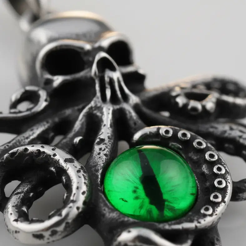 Gros plan sur le pendentif Pieuvre à l’Œil Mystique vert, texture métallique et gemme colorée.